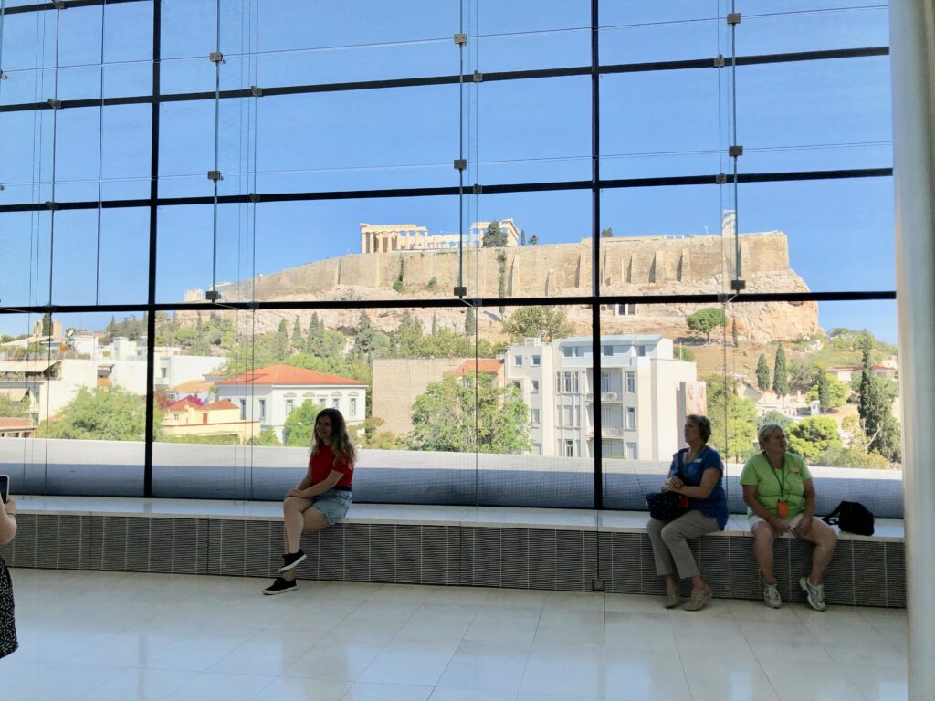 View of the Acropolis seen through a museum window, illustrating how perspective shapes the travel experience.